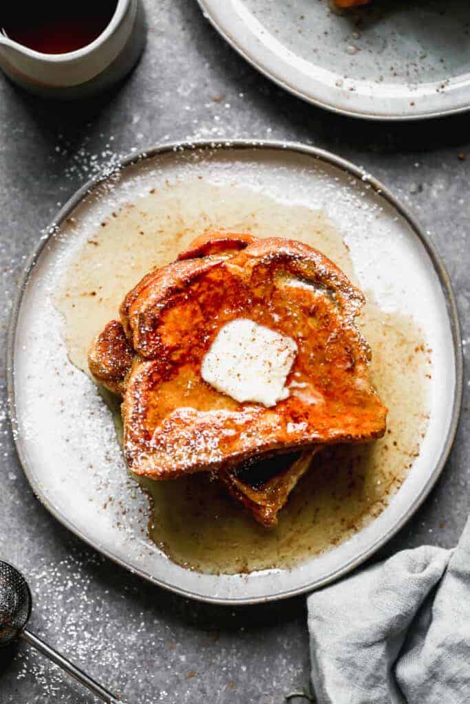 Two slices of pumpkin french toast on a plate, with syrup and butter on top.