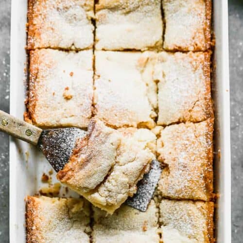 A 9x13 pan of baked gooey butter cake with a spatula removing a piece.