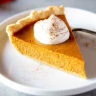 Pumpkin Pie slice with whipped cream on top, on a a plate.