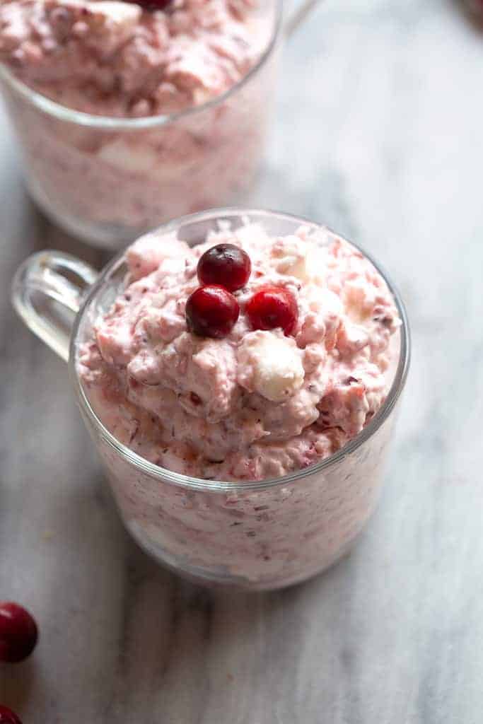 A clear cup full of cranberry salad fluff with three fresh cranberries on top.
