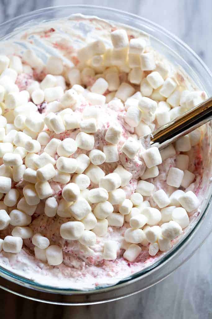Marshmallows added to the top of a cranberry salad in a mixing bowl.
