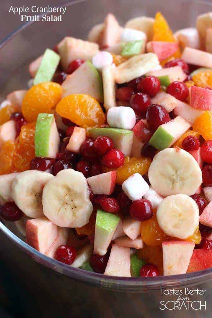 A clear bowl with a fresh fruit salad with bananas, cranberries, mandarin oranges, apples, and mini marshmallows.