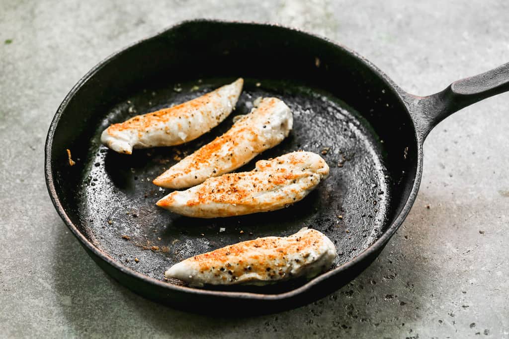Seasoned chicken tenders cooking in a cast iron skillet.