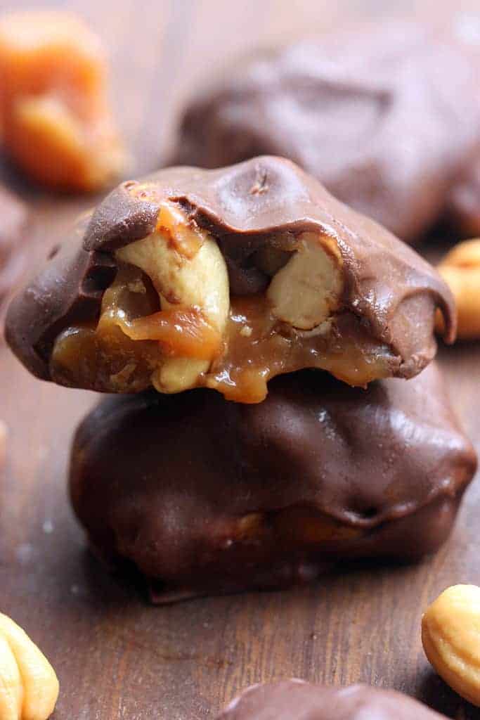 Two caramel cashew clusters stacked on top of each other with a bite taken out of the top one, revealing caramel and cashews.