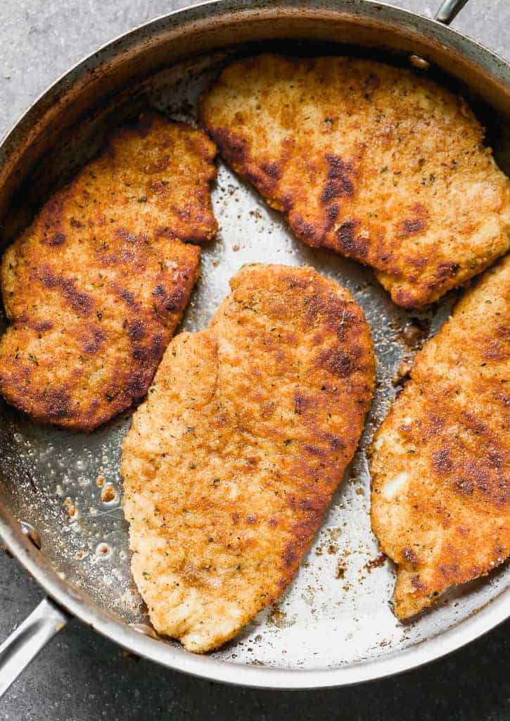 Breaded chicken breasts pan frying in a skillet.