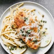 Chicken piccata over cooked spaghetti, on a plate.