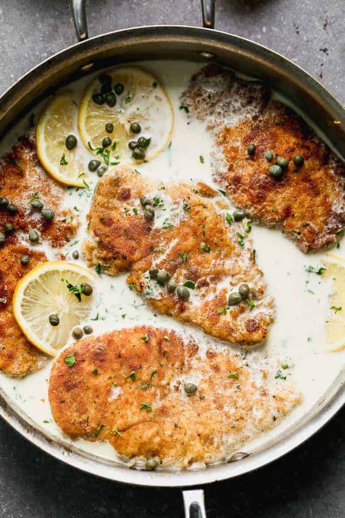 Chicken piccata in a skillet with sauce, capers and lemon slices.