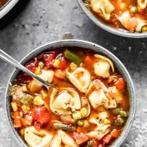 A bowl of Vegetable Tortellini Soup with a spoon in it.