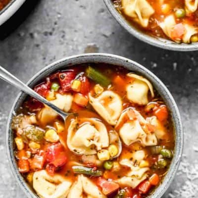 Un bol de soupe de tortellini aux légumes avec une cuillère dedans.