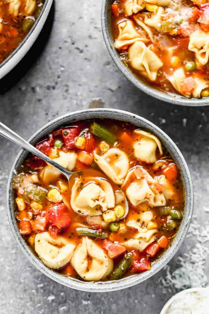 Un bol de soupe de tortellini aux légumes avec une cuillère dedans.