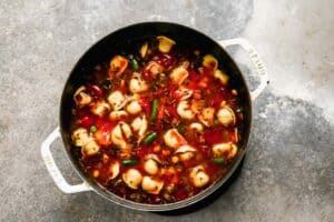 Vegetables and tortellini added to broth in a saucepan to make soup.