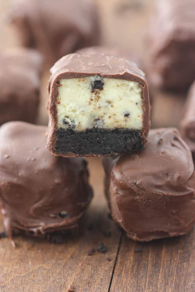 One Oreo cheesecake bite that is cut in half, revealing the filling and oreo crust, stacked on top of two chocolate covered oreo cheesecake bites.