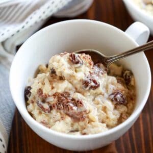 A white cup filled with old fashioned rice pudding with cinnamon and raisins and a spoon.