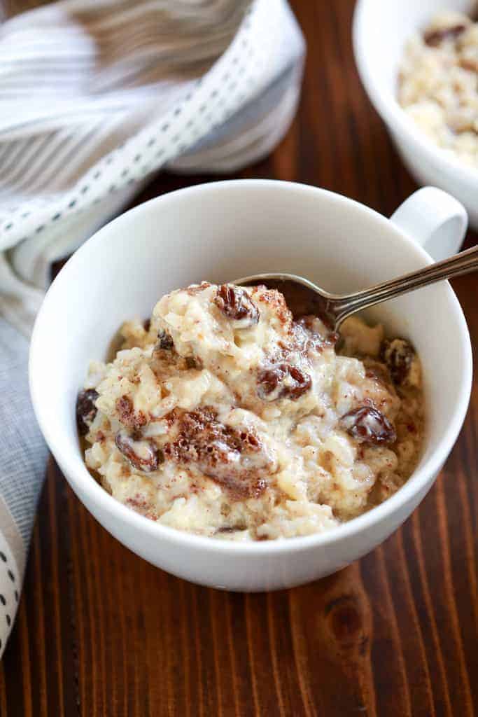 A white cup filled with old fashioned rice pudding with cinnamon and raisins and a spoon. 