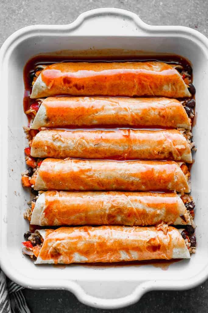 Vegetarian enchiladas in a pan with enchilada sauce poured on top.