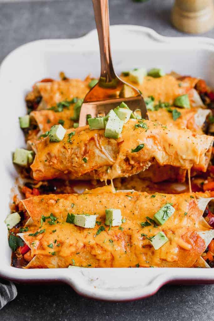 Vegetarian Enchiladas in a pan with a spatula lifting one up.