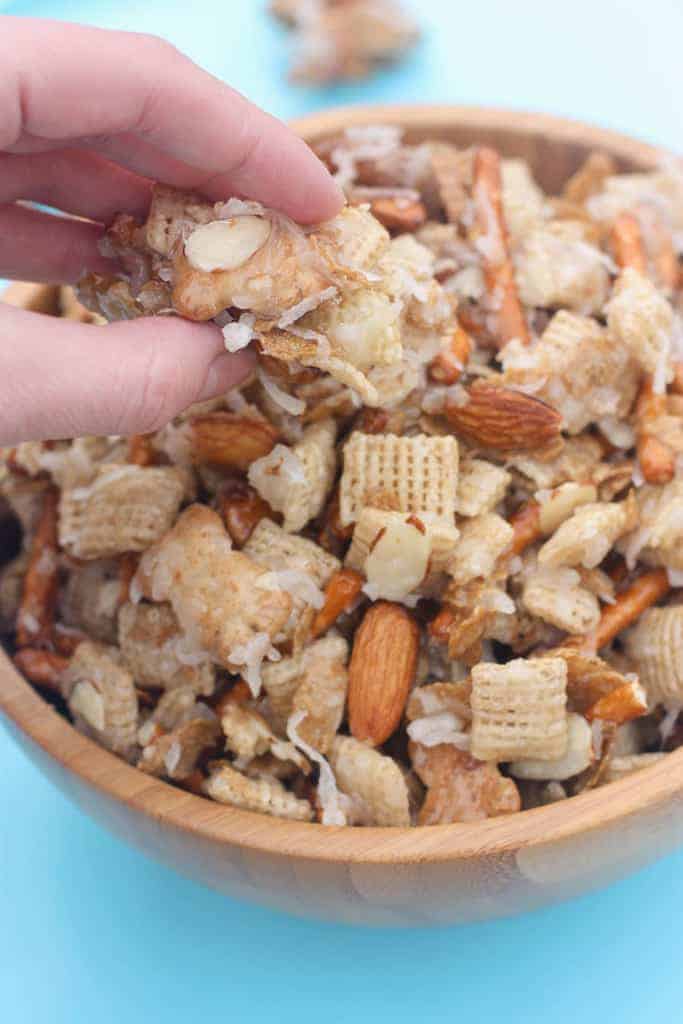 A hand reaching in to a bowl to grab a pinch of almond coconut Chex mix.
