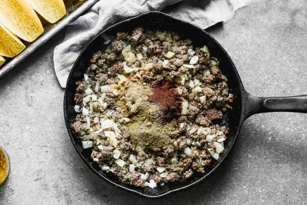 Cooked ground beef and onion in a skillet with taco seasoning spices added on top.