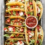 Baked Tacos lined on a baking tray, topped with salsa, sour cream and lettuce.