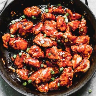 Una sartén con Pollo General Tso casero, adornado con cebolla verde picada.