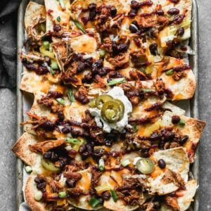 A sheet pan with pulled pork nachos on it and a scoop of sour cream topped on them in the middle.