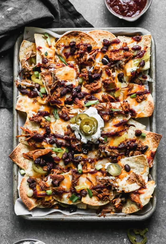 A sheet pan with pulled pork nachos on it and a scoop of sour cream topped on them in the middle.