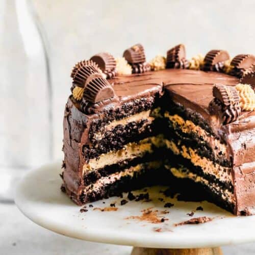 A cake stand displaying a Chocolate peanut butter cake with a few slices removed, showing the layers inside. .