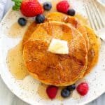 Three whole wheat pancakes on a speckled plate with berries and syrup on top.
