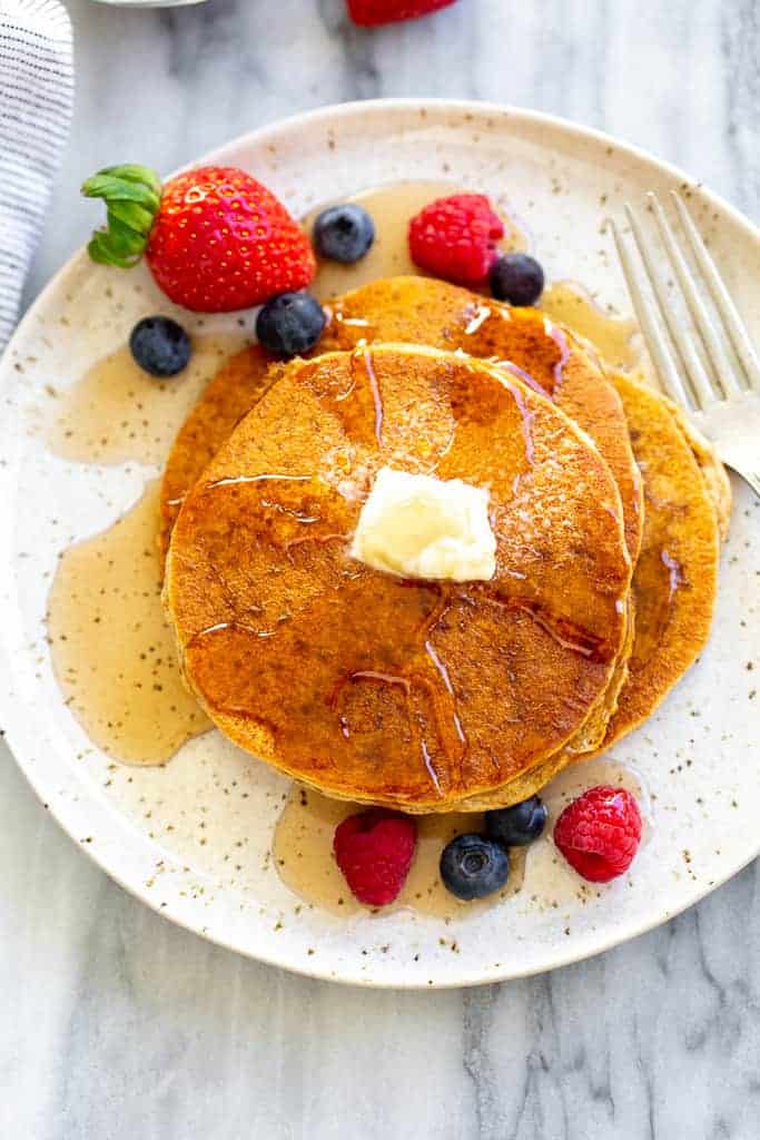 Three whole wheat pancakes on a speckled plate with berries and syrup on top.