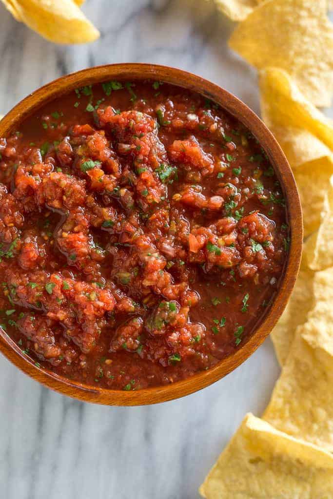 Overhead photo of a wooden bowl filled with homemade Mexican salsa with tortilla chips on the side.