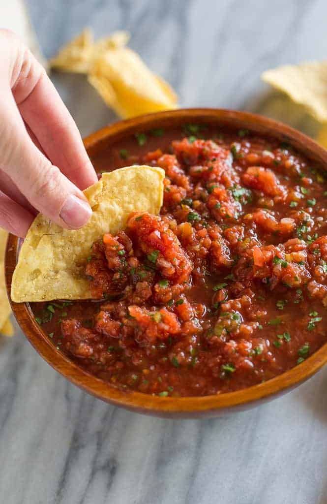 A chip scooping some salsa from a bowl of homemade salsa.