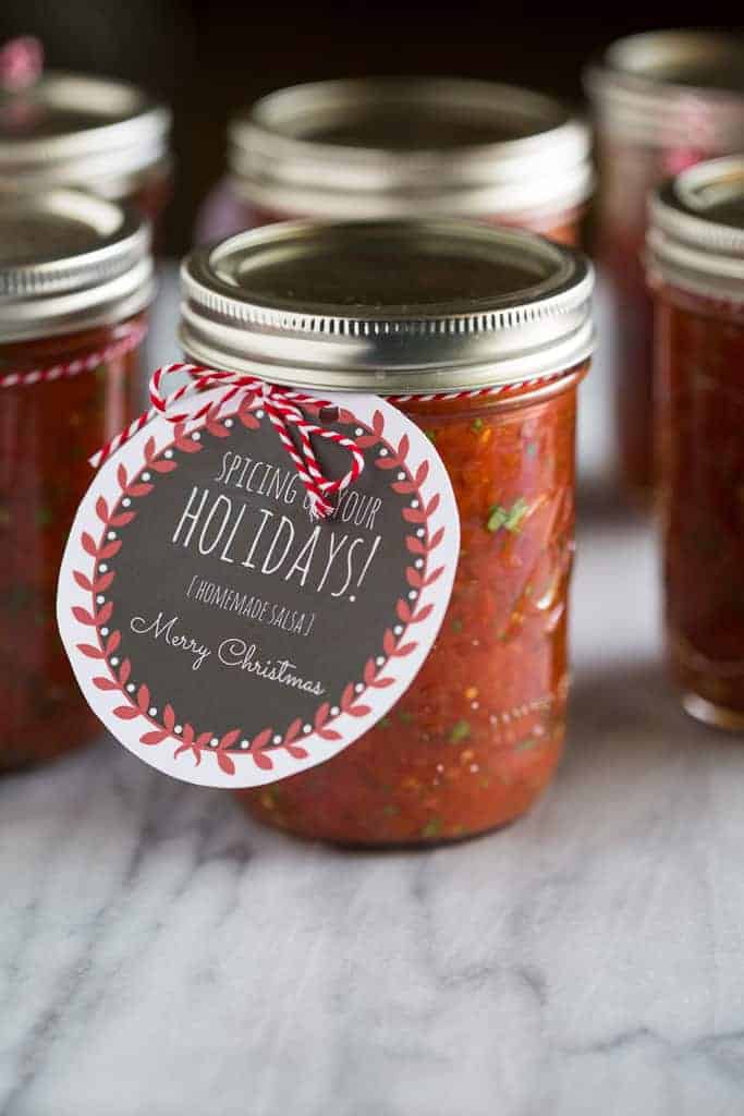 A pint jar of homemade salsa with a Christmas gift tag tied on it and more pint jars in the background.