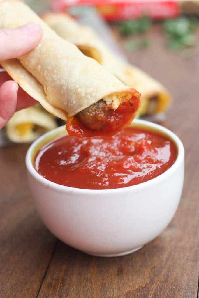 One Egg and Sausage Breakfast Taquitos being dunked in a small white saucer filled with salsa.