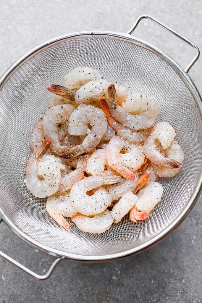 Raw uncooked shrimp in a fine mesh strainer.