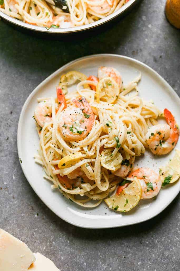 Shrimp scampi served over cooked pasta, on a plate.
