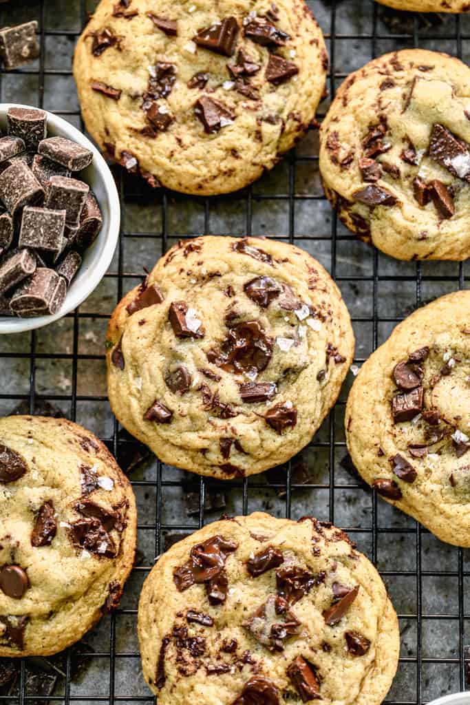 Freshly baked Browned Butter Chocolate Chip Cookies on a cooling rack with a small bowl of chocolate chunks.