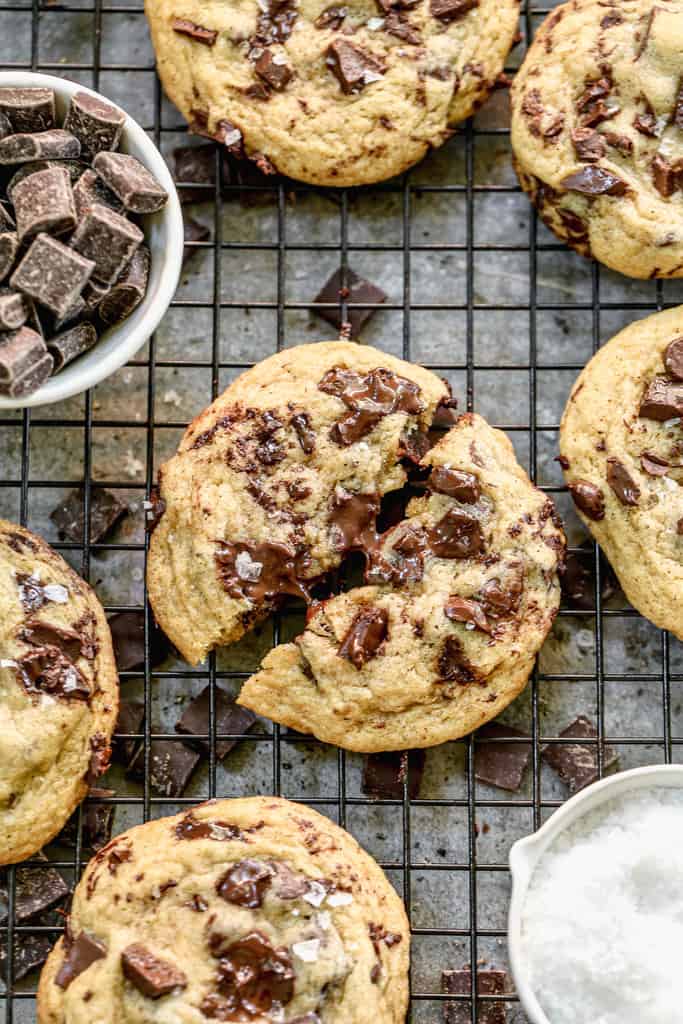 Browned Butter Chocolate Chip Cookies on a cooling rack with a small bowl of chocolate chips, and one cookie broken in half.