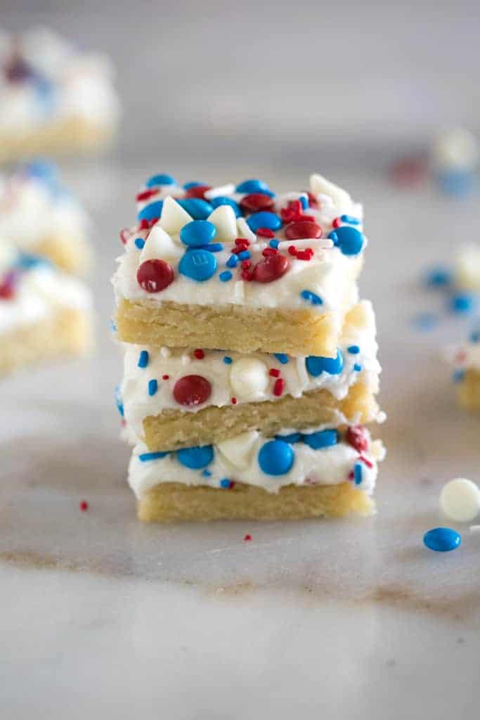 Three stacked, frosted sugar cookie bars decorated with red, white and blue sprinkles and candy on top.