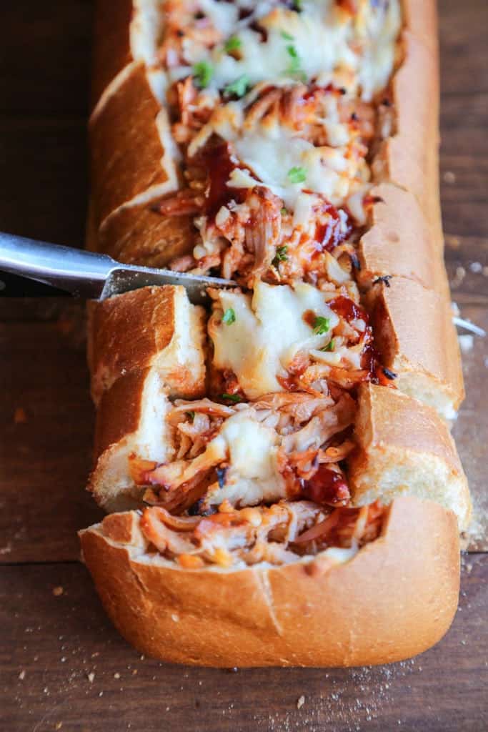 A large baguette filled with BBQ Chicken being cut into slices.
