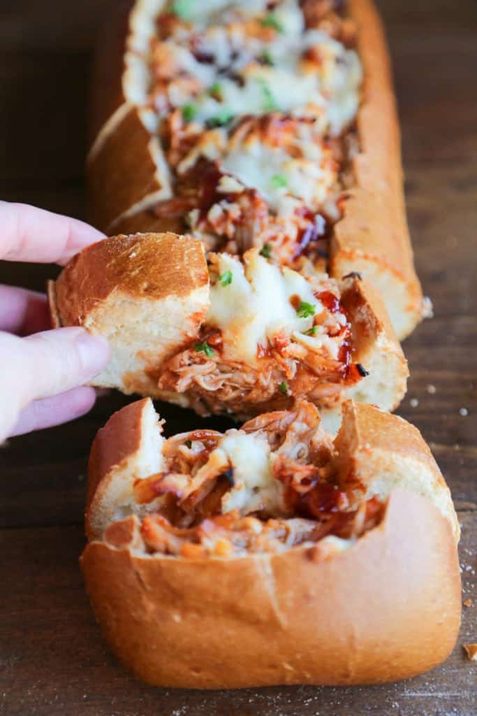 A person removing a slice of BBQ Chicken Stuffed Bread from the rest of the baguette.