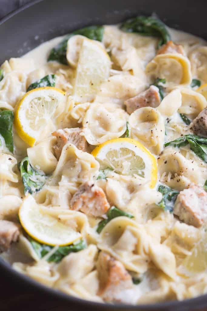 A pan filled with tortellini, chicken pieces, spinach and a creamy lemon sauce.