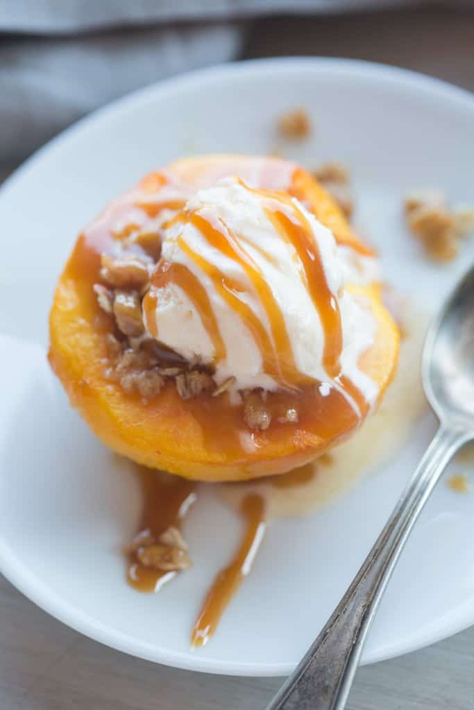 A half of a baked peach topped with a crumbled oat mixture, ice cream, and caramel.