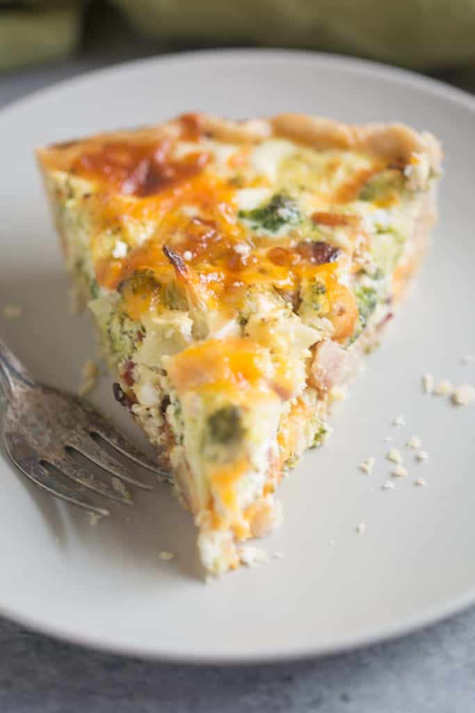 A triangular slice of a Broccoli Cheese Quiche with small pieces of bacon and broccoli sitting on a white plate.