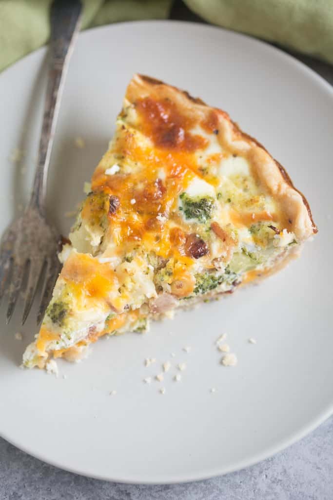 An overhead view of a triangular slice of a broccoli cheese quiche with bacon bits and a homemade crust.