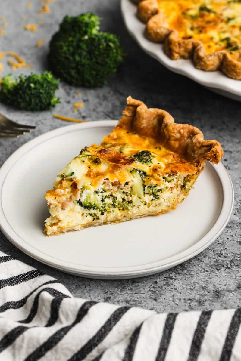 A slice of a broccoli and cheddar quiche recipe on a plate, cooked until golden and ready to serve.