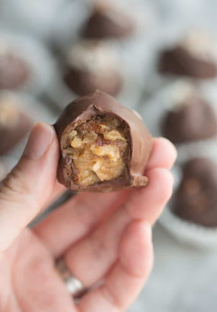 A hand holding a German Chocolate Truffles that has a bite taken out to reveal the german chocolate filling.