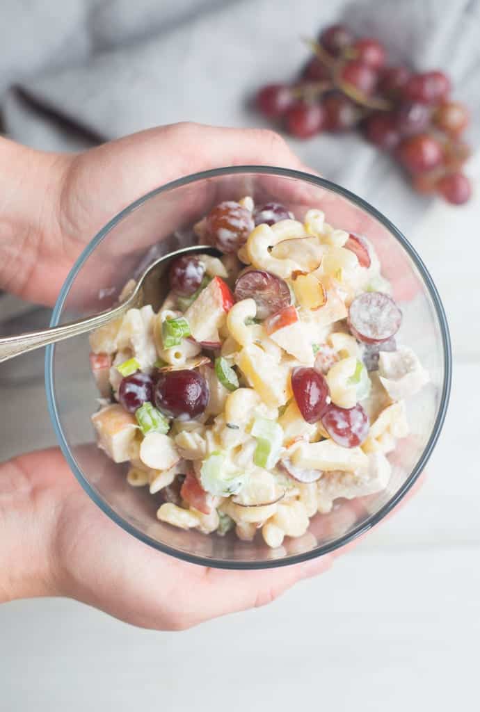 Two hands holding a bowl of Macaroni Fruit Salad with a spoon sticking out.