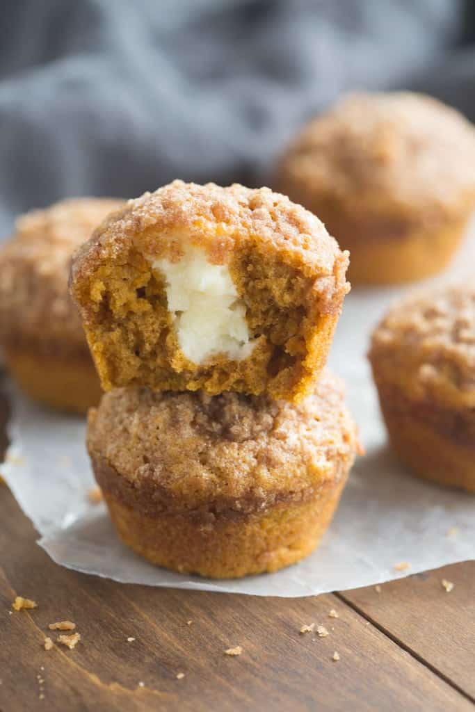 A pumpkin muffin that has had a bite taken out of it, revealing a cream cheese filling.