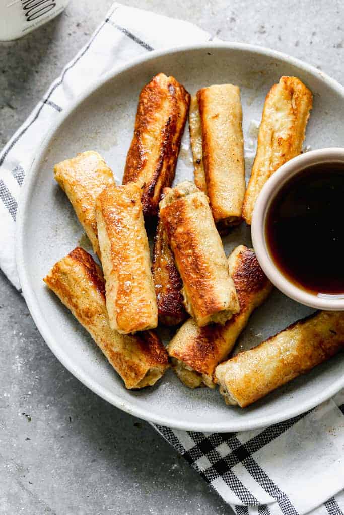 French Toast Roll-ups served on a plate with a small bowl of syrup, for dipping.
