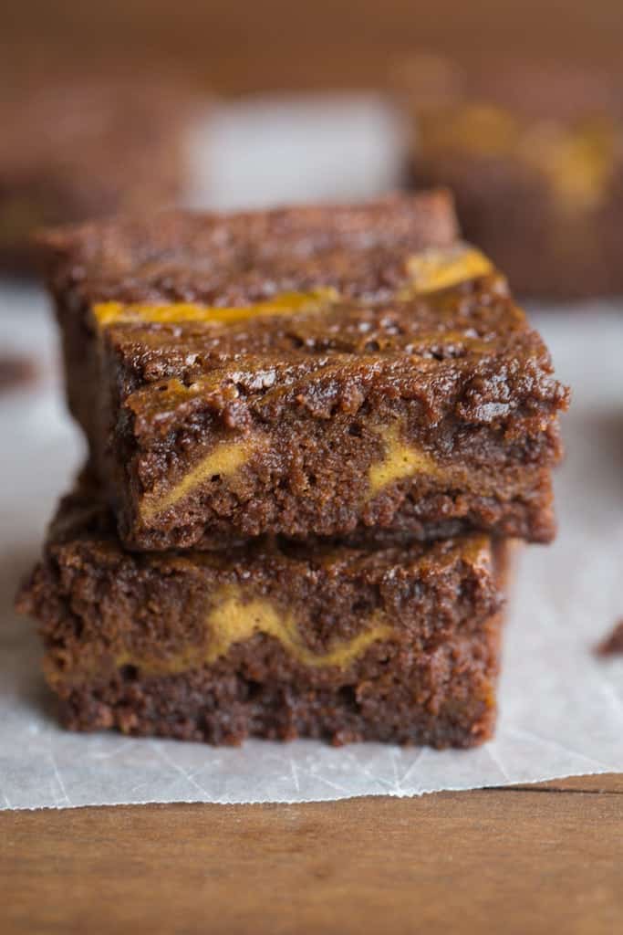 Two chocolate brownies with with orange pumpkin swirl, stacked on top of each other.